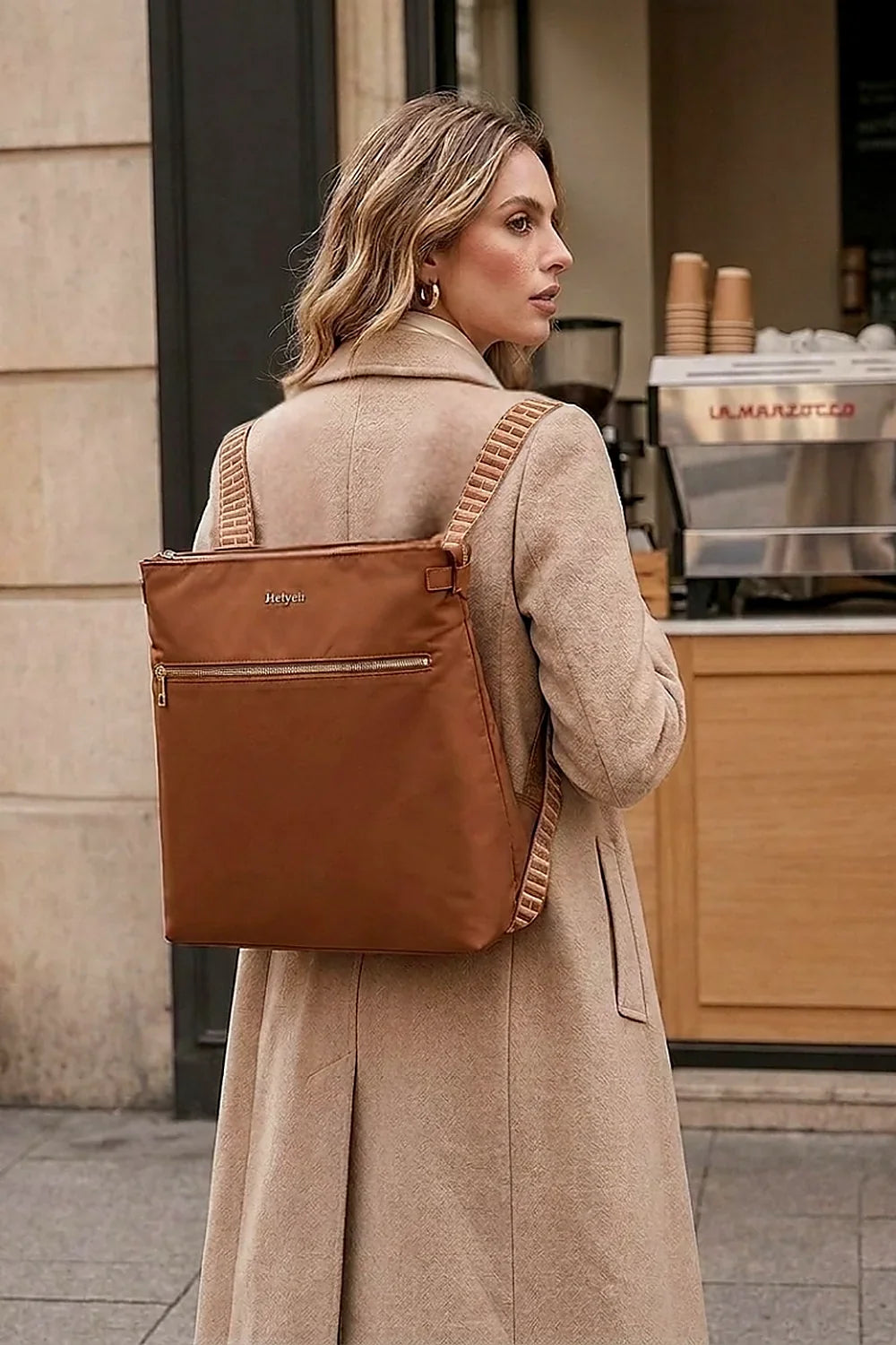 Woman wearing a cognac Heiych convertible tote backpack in backpack mode on a city street