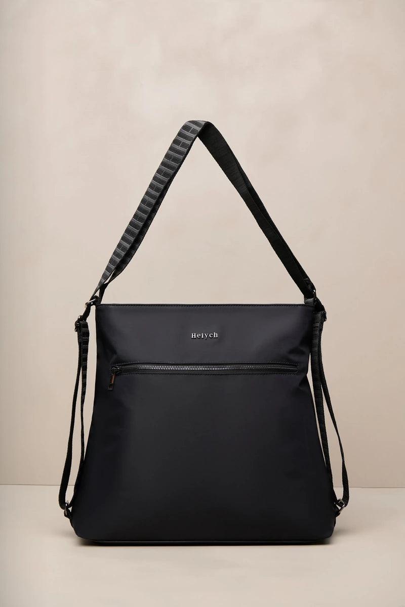 A black nylon shoulder bag with a wide, ribbed black strap, a front zippered pocket, and a small silver 'Heiych' logo on the front, set against a neutral beige background.