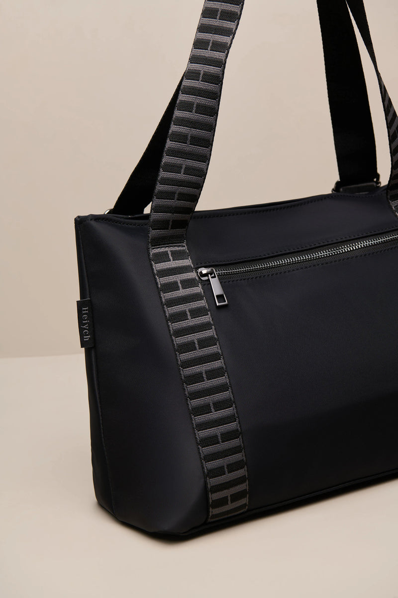 A black nylon duffel bag with a distinctive black-and-gray brick-patterned shoulder strap, shown on a neutral beige background.