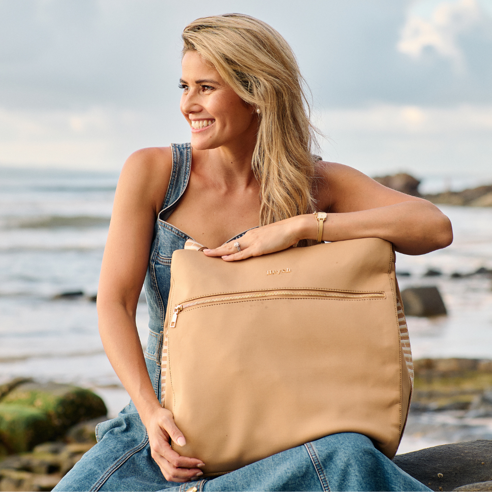 Designer and Founder Laura King holding Tan neoprene tote bag at the beach