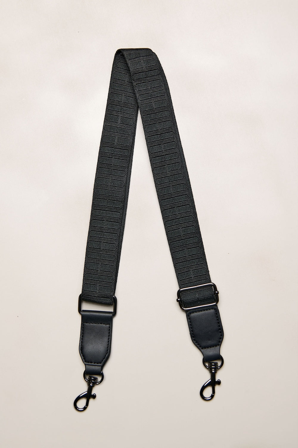 Black bag strap with metal hardware on a beige background