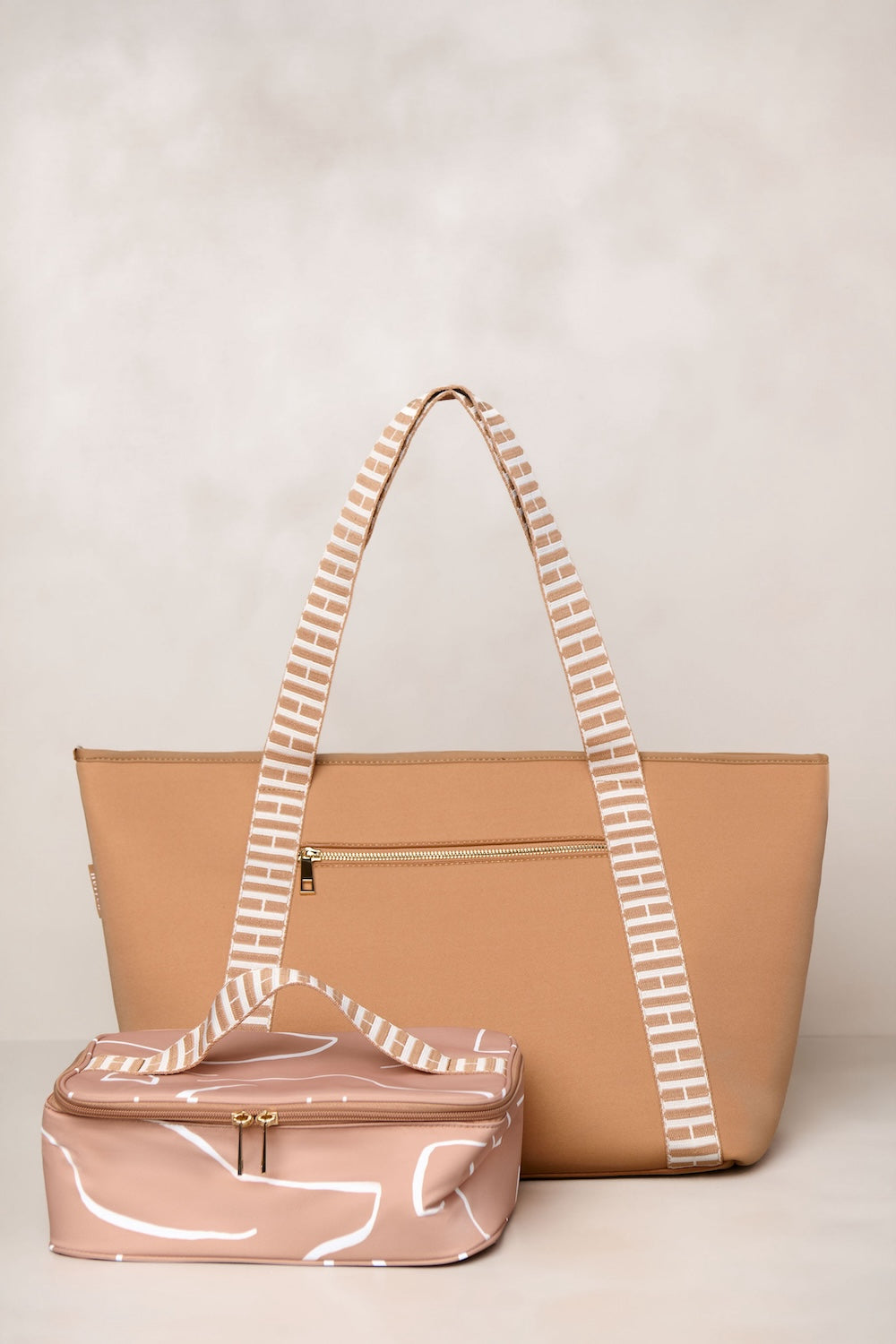 Tan tote bag with striped handle and tan vanity case on a beige background