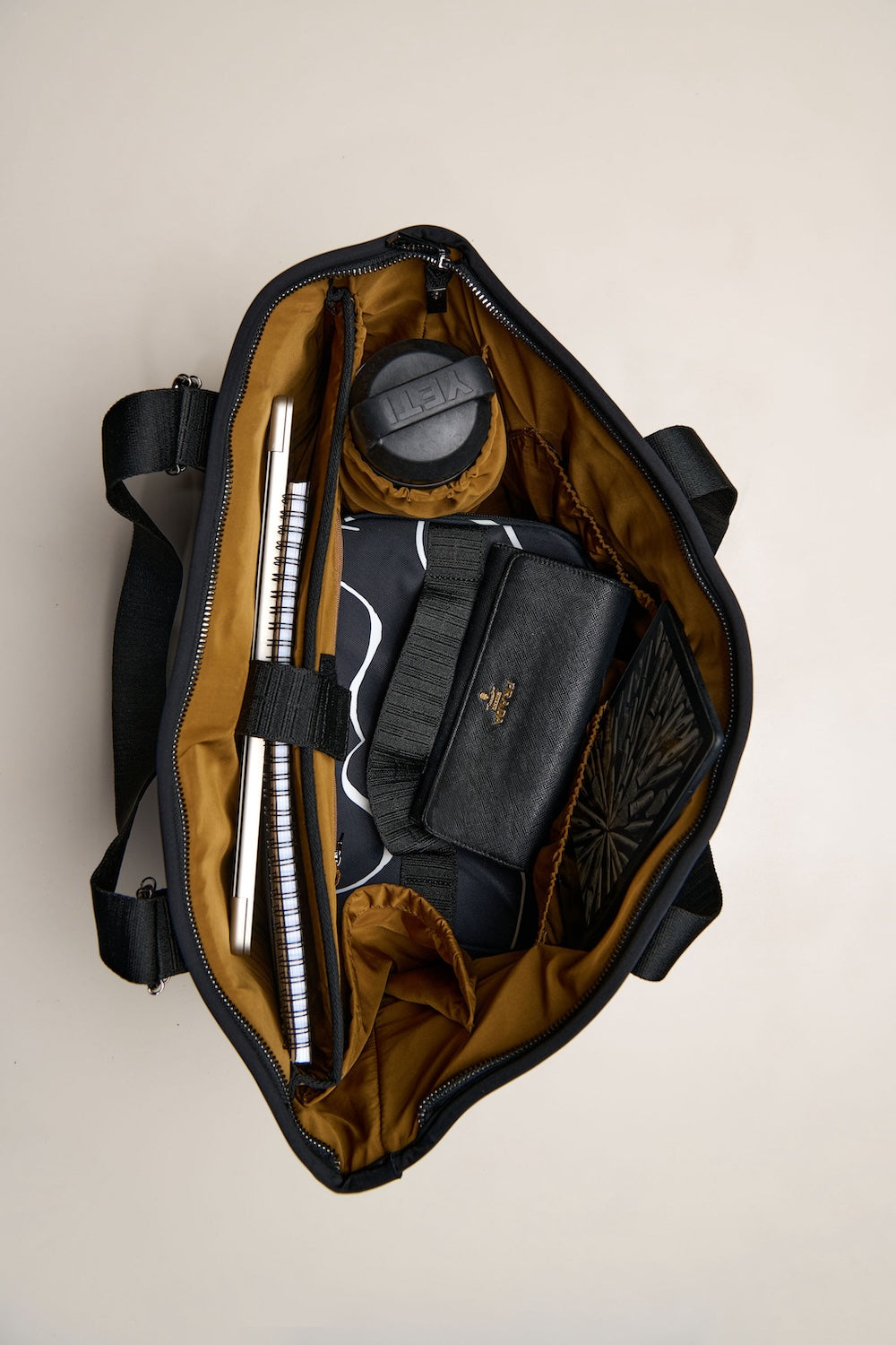 Open black duffel bag with travel items on a beige background
