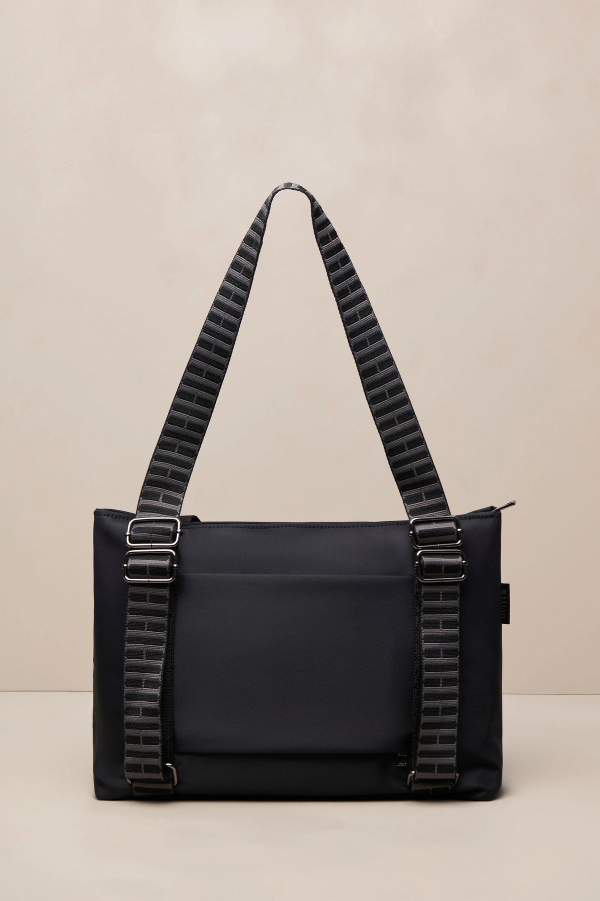 A black nylon shoulder bag with distinctive ribbed black straps and silver-tone hardware, set against a neutral beige background.
