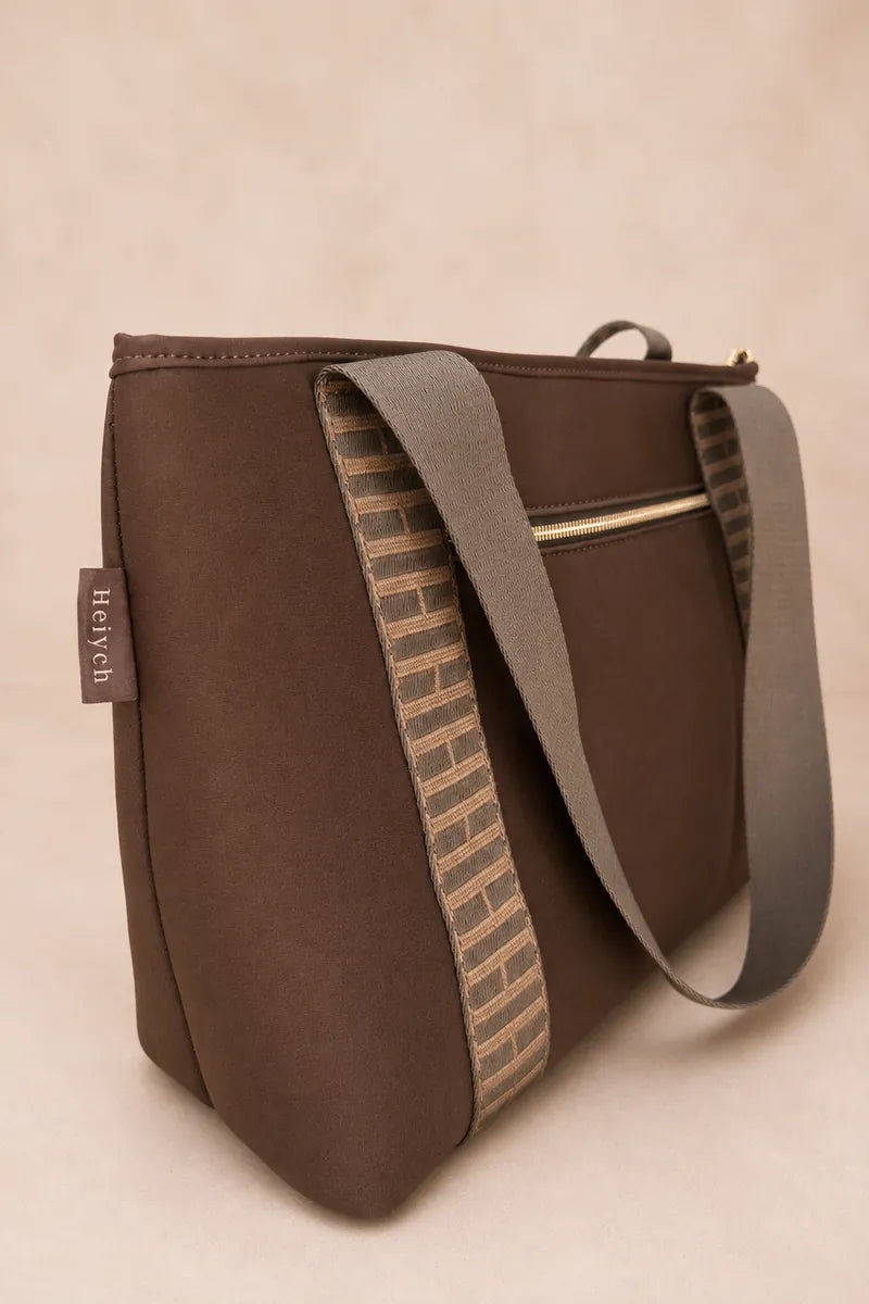A chocolate brown fabric shoulder bag with a wide brown strap featuring a beige and brown brick pattern, set against a warm beige background.