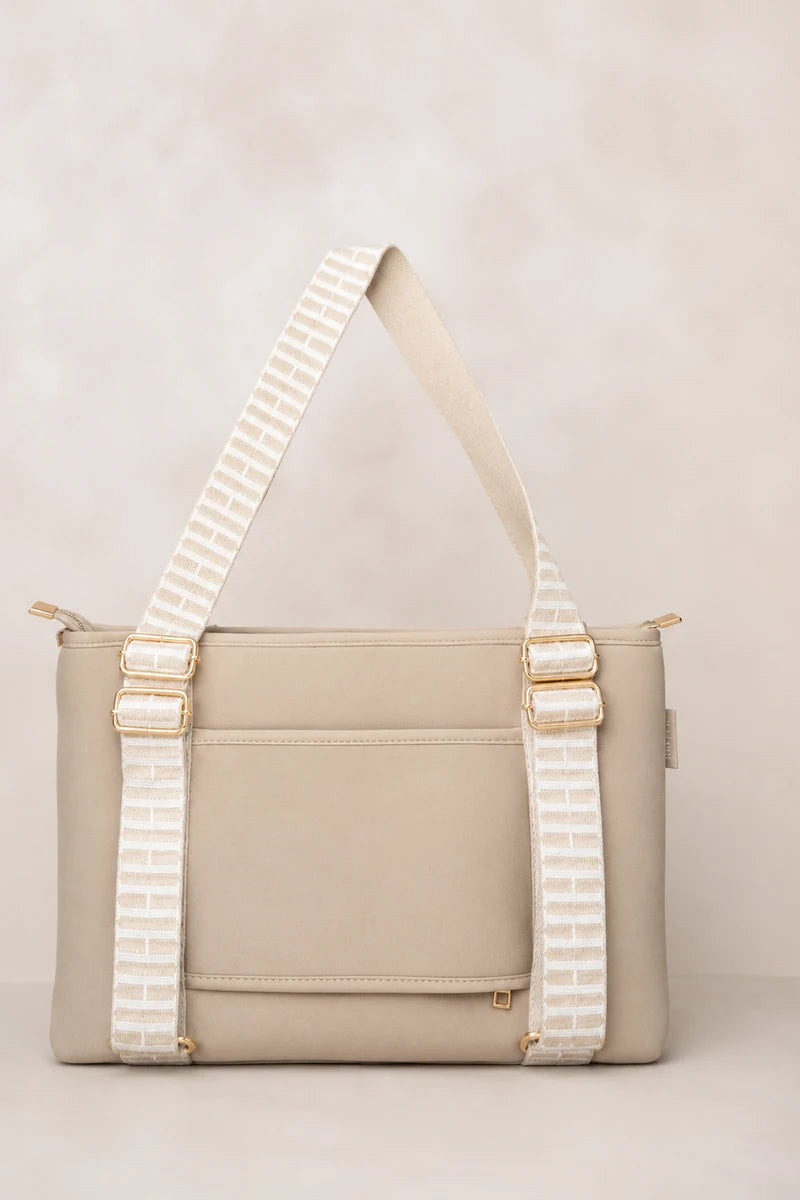 A structured taupe beige shoulder bag with a wide, patterned cream strap featuring gold-tone hardware, set against a neutral beige background.