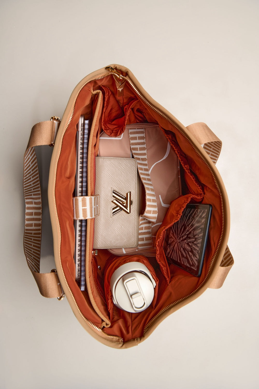 Open tan bag with various items on a light gray background